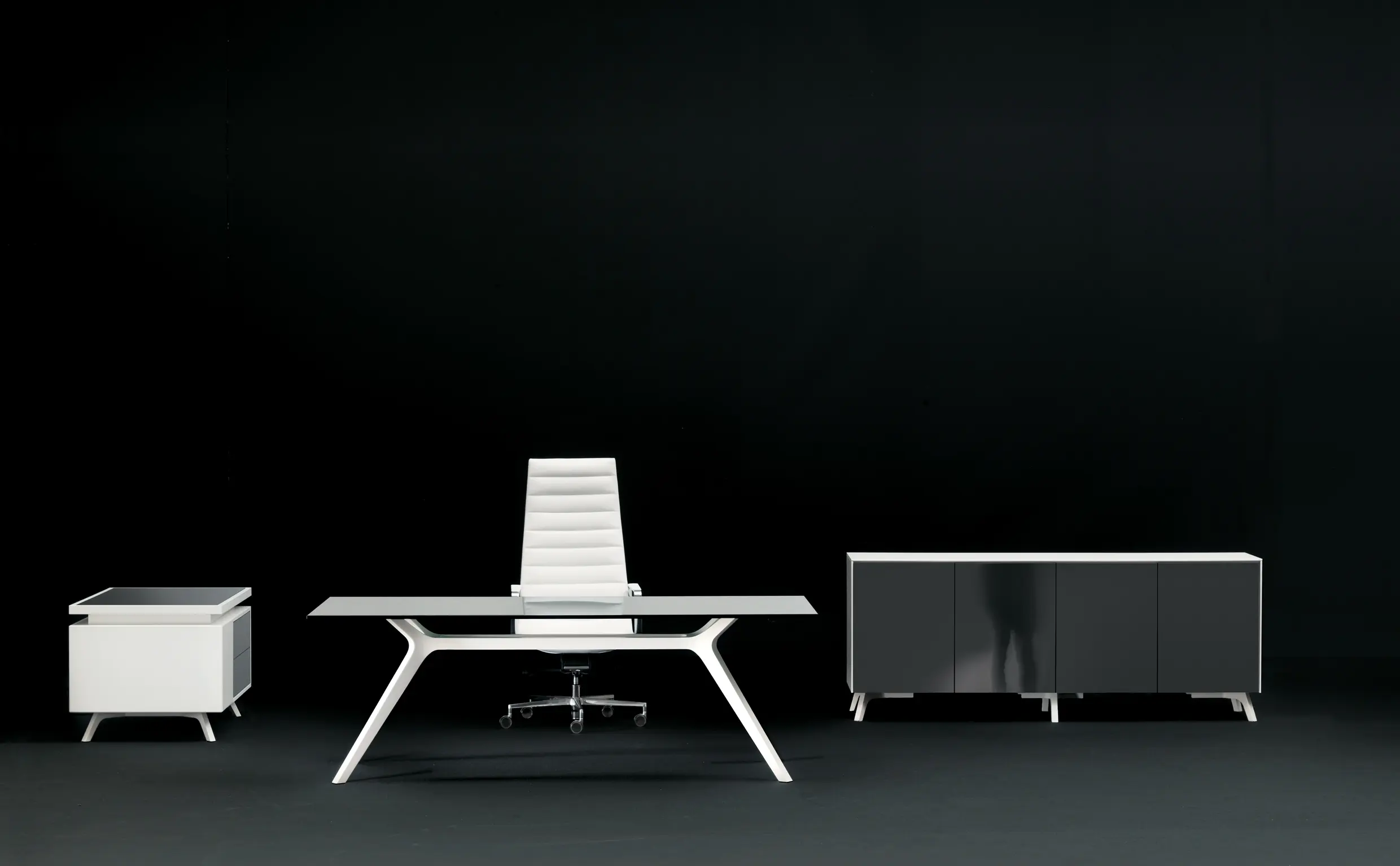 DEKKO Interiors | Αισθητική & Εργονομία στα Έπιπλα Γραφείου Η κατασκευή του γραφείου αποπνέει μια ευάερη και δυναμική αίσθηση, χάρη στην ξύλινη δομή του, η οποία είναι εμπνευσμένη από το στυλ "Mollinian". Αυτή η μοναδική κατασκευή στηρίζει είτε μια γυάλινη είτε μια ξύλινη επιφάνεια σε μια εντυπωσιακή ισορροπία αντίθετων δυνάμεων, δημιουργώντας ένα εντυπωσιακό οπτικό αποτέλεσμα. Το πολύτιμο ξύλο καρυδιάς παίζει κεντρικό ρόλο στον σχεδιασμό του γραφείου. Η επιφάνεια εργασίας, κατασκευασμένη από φυσικό καρυδιά ξύλο, είναι το αποκορύφωμα της υλικότητας και της χειροτεχνίας, με ένα συμπαγές προφίλ και στρογγυλεμένες άκρες που αναδεικνύουν τη φυσική ομορφιά του υλικού. Η γοητεία του κρυστάλλου συναντά την ισχυρή και στιβαρή αίσθηση του μαόνι kotibé στη δομή του γραφείου. Προτείνεται σε δύο εκδόσεις: λευκή και ανθρακί λάκα, προσφέροντας έτσι ευελιξία στον σχεδιασμό του εσωτερικού χώρου. Οι κρυστάλλινες επιφάνειες είναι διαθέσιμες σε τρεις εκδόσεις: εξαιρετικά διαφανές γυαλί, λευκό λακαρισμένο γυαλί, και καπνιστό γυαλί, όλα πάχους 15 mm, προσδίδοντας μία επιπλέον διάσταση πολυτέλειας.