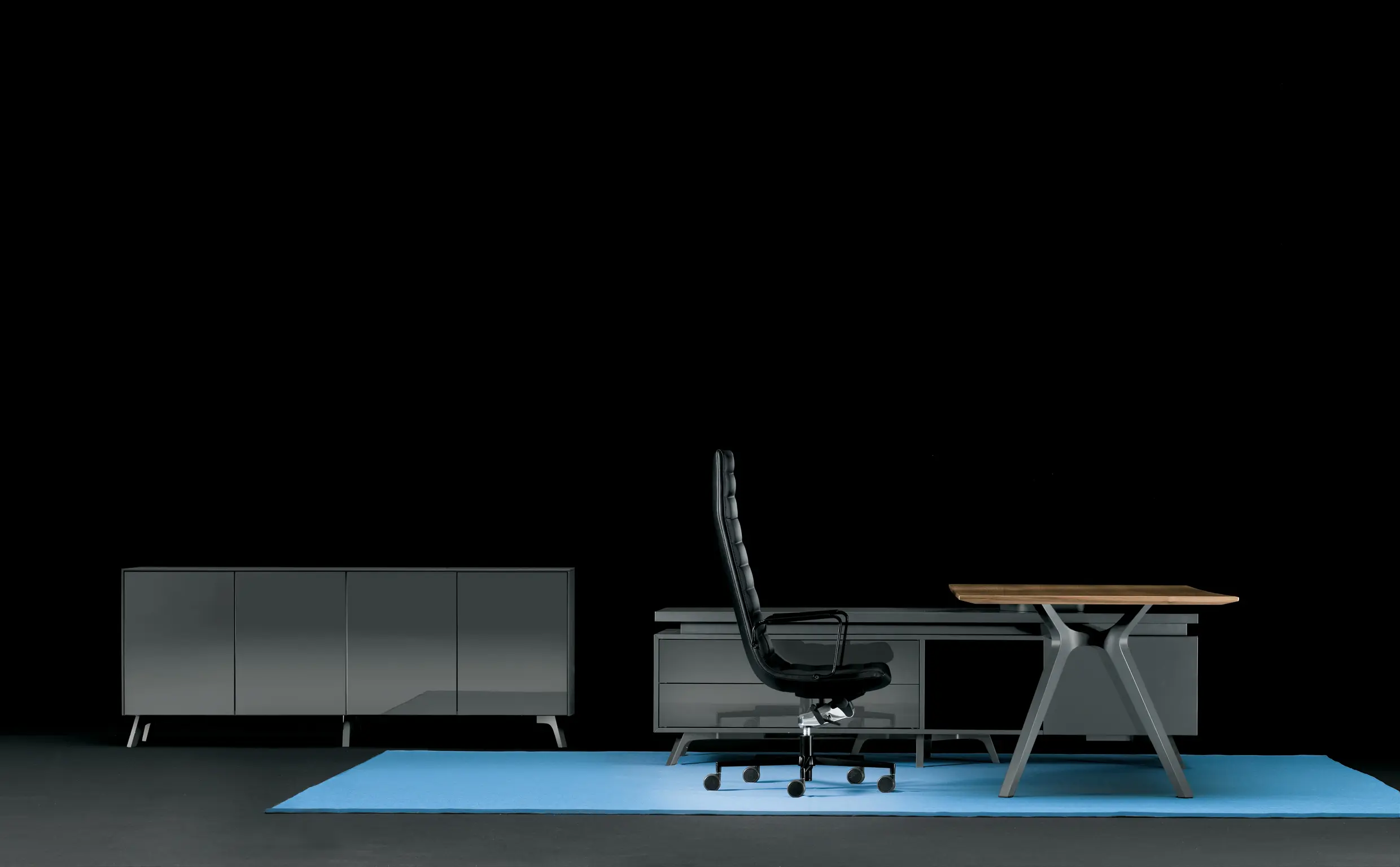 DEKKO Interiors | Αισθητική & Εργονομία στα Έπιπλα Γραφείου Η κατασκευή του γραφείου αποπνέει μια ευάερη και δυναμική αίσθηση, χάρη στην ξύλινη δομή του, η οποία είναι εμπνευσμένη από το στυλ "Mollinian". Αυτή η μοναδική κατασκευή στηρίζει είτε μια γυάλινη είτε μια ξύλινη επιφάνεια σε μια εντυπωσιακή ισορροπία αντίθετων δυνάμεων, δημιουργώντας ένα εντυπωσιακό οπτικό αποτέλεσμα. Το πολύτιμο ξύλο καρυδιάς παίζει κεντρικό ρόλο στον σχεδιασμό του γραφείου. Η επιφάνεια εργασίας, κατασκευασμένη από φυσικό καρυδιά ξύλο, είναι το αποκορύφωμα της υλικότητας και της χειροτεχνίας, με ένα συμπαγές προφίλ και στρογγυλεμένες άκρες που αναδεικνύουν τη φυσική ομορφιά του υλικού. Η γοητεία του κρυστάλλου συναντά την ισχυρή και στιβαρή αίσθηση του μαόνι kotibé στη δομή του γραφείου. Προτείνεται σε δύο εκδόσεις: λευκή και ανθρακί λάκα, προσφέροντας έτσι ευελιξία στον σχεδιασμό του εσωτερικού χώρου. Οι κρυστάλλινες επιφάνειες είναι διαθέσιμες σε τρεις εκδόσεις: εξαιρετικά διαφανές γυαλί, λευκό λακαρισμένο γυαλί, και καπνιστό γυαλί, όλα πάχους 15 mm, προσδίδοντας μία επιπλέον διάσταση πολυτέλειας.